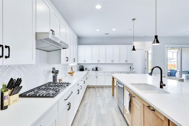 kitchen featuring backsplash, under cabinet range hood, light countertops, appliances with stainless steel finishes, and a sink