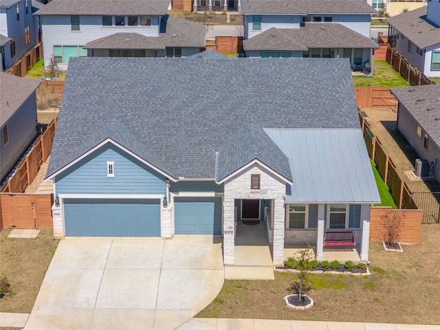 view of front of home featuring a shingled roof, concrete driveway, metal roof, a garage, and stone siding