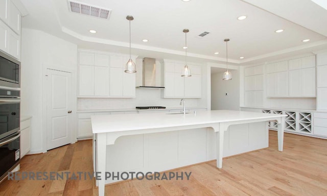 kitchen with a tray ceiling, wall chimney exhaust hood, visible vents, and a sink