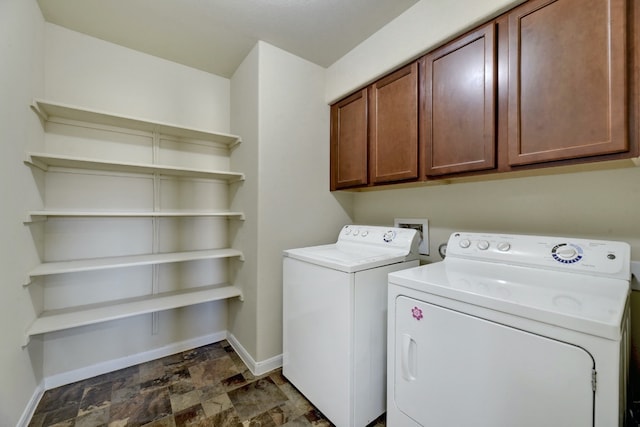 washroom featuring stone finish floor, washing machine and dryer, cabinet space, and baseboards