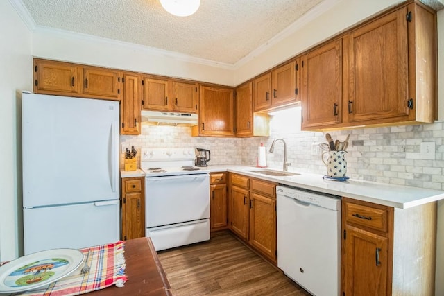 kitchen with a sink, under cabinet range hood, white appliances, crown molding, and dark wood-style flooring