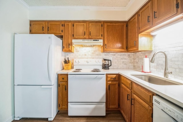 kitchen with white appliances, brown cabinetry, ornamental molding, a sink, and under cabinet range hood