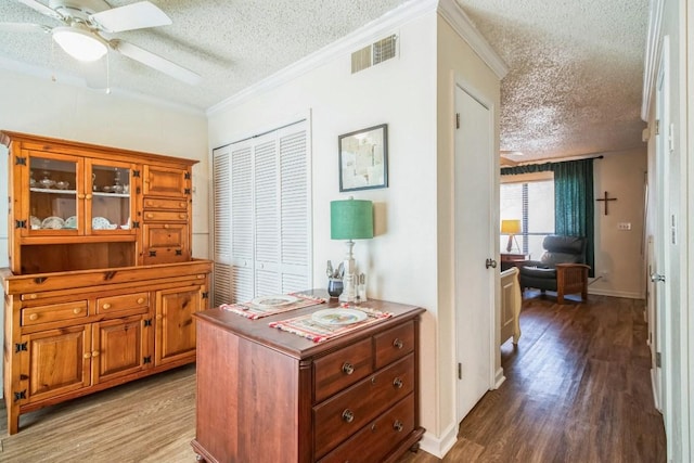 hall with visible vents, a textured ceiling, wood finished floors, crown molding, and baseboards