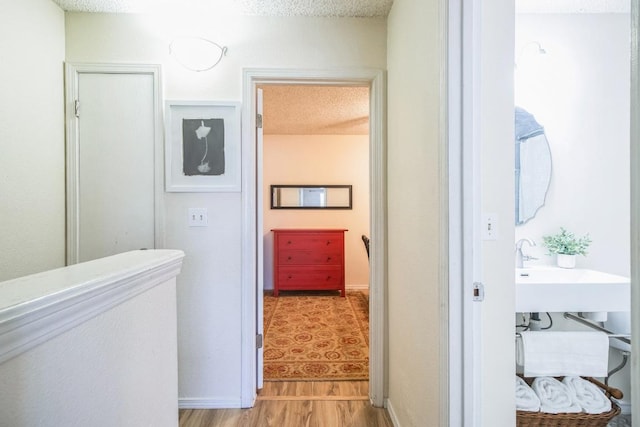 corridor with light wood-style floors, baseboards, and a textured ceiling