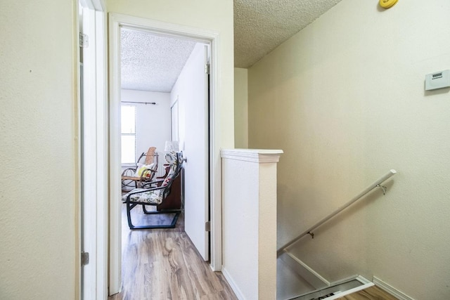 corridor featuring an upstairs landing, a textured ceiling, baseboards, and wood finished floors