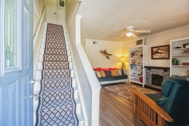 interior space featuring ceiling fan, stairs, a fireplace, wood finished floors, and a textured ceiling