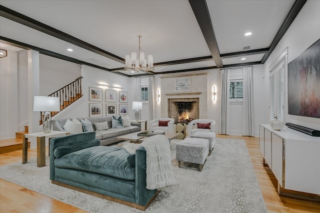 living room featuring stairway, beam ceiling, light wood-style flooring, a brick fireplace, and a notable chandelier