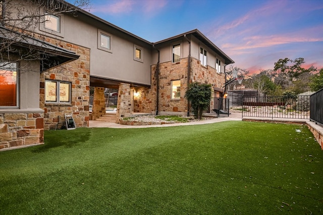 rear view of house with stucco siding, stone siding, a lawn, and fence