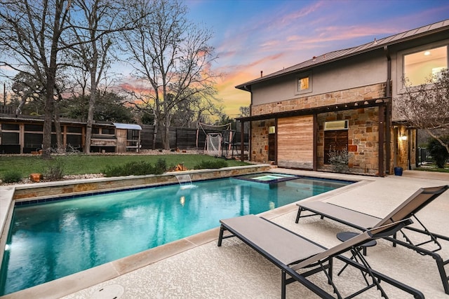 pool at dusk featuring a patio, fence, a yard, an outdoor pool, and an in ground hot tub