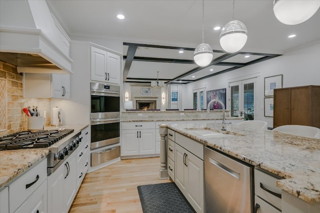 kitchen featuring premium range hood, appliances with stainless steel finishes, white cabinets, a warming drawer, and a sink