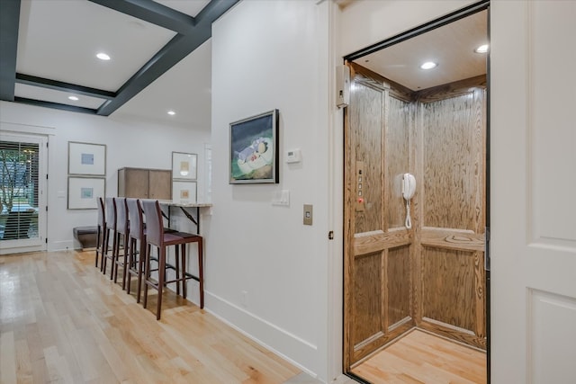 interior space featuring beamed ceiling, elevator, baseboards, and light wood finished floors