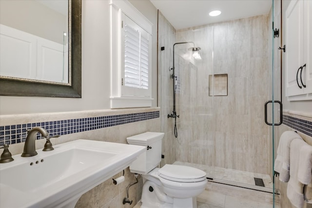 bathroom with a sink, toilet, tile walls, and a shower stall