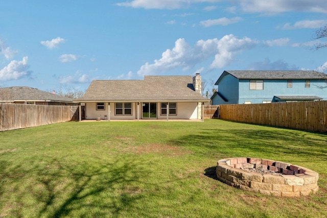 back of property featuring a lawn, a fenced backyard, a chimney, and an outdoor fire pit