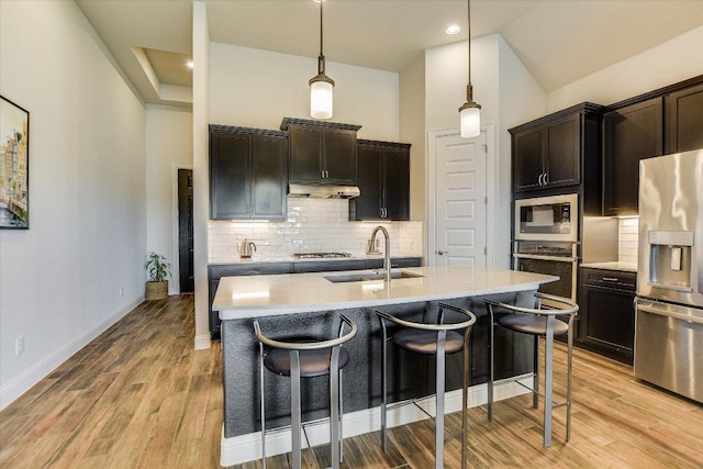 kitchen featuring a sink, decorative backsplash, stainless steel appliances, under cabinet range hood, and a kitchen bar