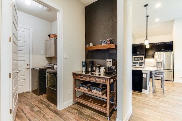 interior space with light wood finished floors, light countertops, appliances with stainless steel finishes, a kitchen breakfast bar, and separate washer and dryer