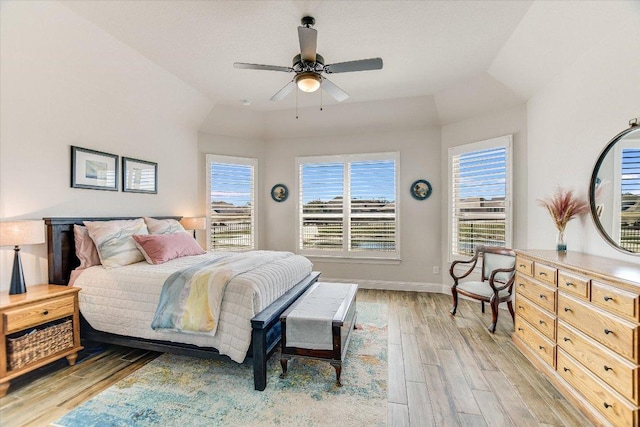 bedroom featuring a tray ceiling, baseboards, light wood-type flooring, and ceiling fan