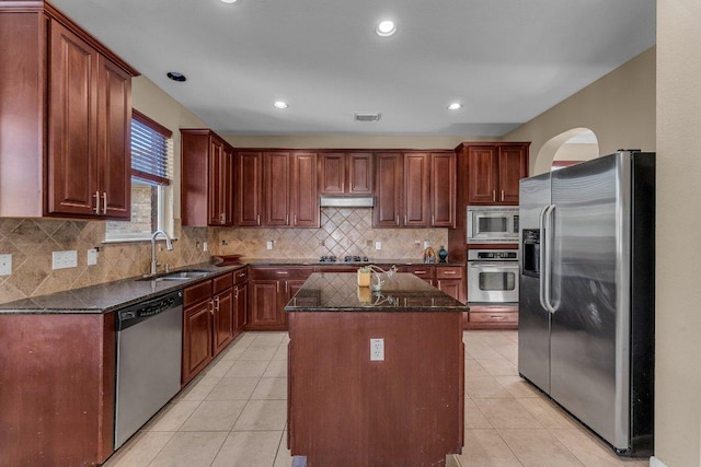 kitchen featuring dark stone countertops, a kitchen island, light tile patterned flooring, a sink, and appliances with stainless steel finishes