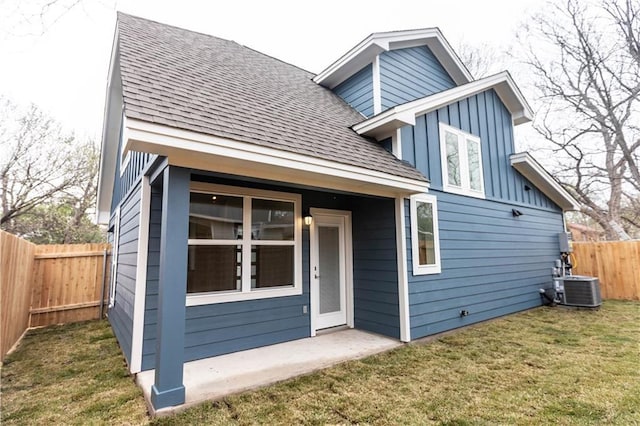 view of front of home with roof with shingles, a fenced backyard, central AC, a front lawn, and board and batten siding