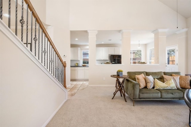 living area with a high ceiling, decorative columns, light colored carpet, and baseboards