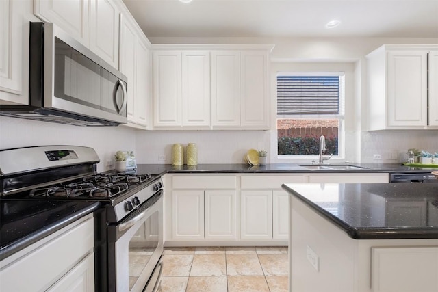 kitchen with a sink, dark stone counters, white cabinets, and stainless steel appliances