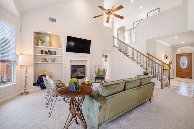 carpeted living area with visible vents, high vaulted ceiling, stairway, ceiling fan, and a tile fireplace