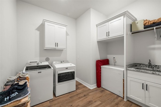 laundry area with a sink, cabinet space, light wood-style floors, separate washer and dryer, and baseboards