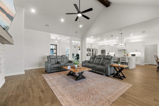 living room featuring baseboards, beam ceiling, ceiling fan with notable chandelier, light wood-style floors, and high vaulted ceiling