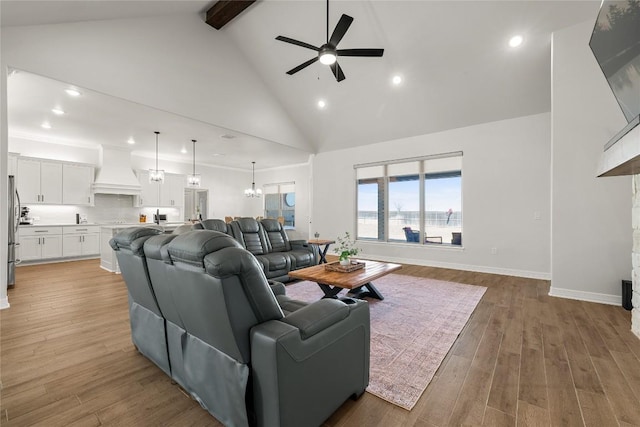 living room with baseboards, beam ceiling, ceiling fan with notable chandelier, light wood-style floors, and high vaulted ceiling