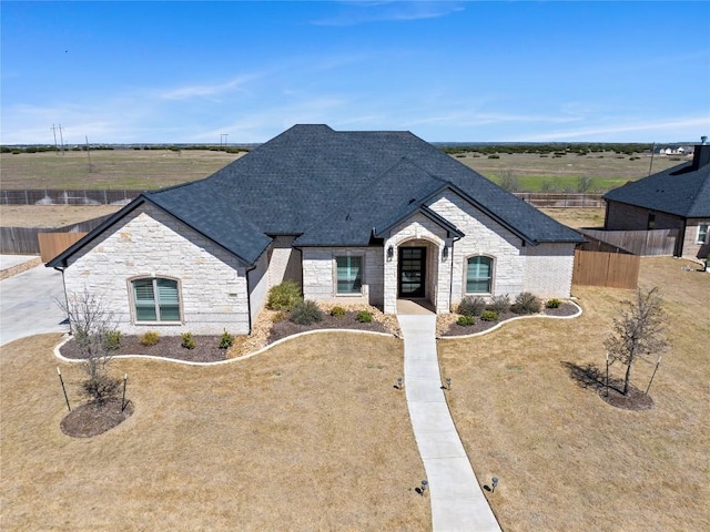 french country home with stone siding, roof with shingles, and fence