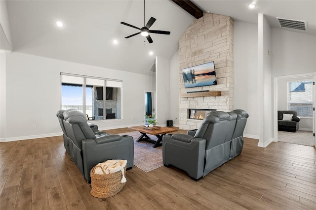 living area featuring wood finished floors, visible vents, high vaulted ceiling, a fireplace, and beamed ceiling