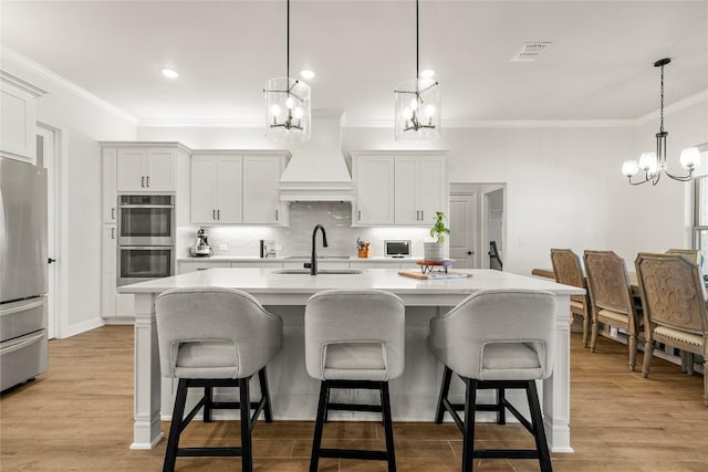 kitchen with visible vents, custom exhaust hood, light wood-style flooring, a sink, and appliances with stainless steel finishes