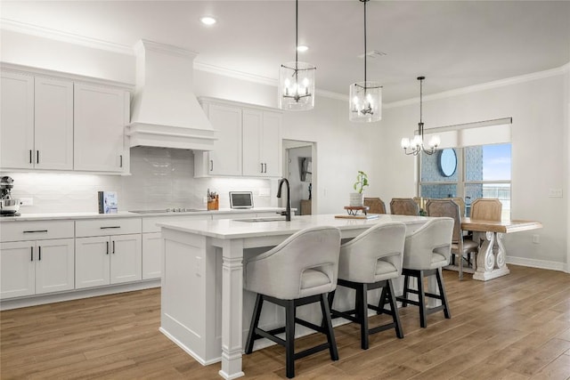 kitchen with a kitchen bar, light wood-style flooring, custom range hood, light countertops, and decorative backsplash