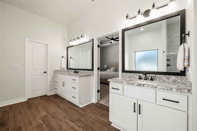 ensuite bathroom with walk in shower, two vanities, wood finished floors, a ceiling fan, and a sink