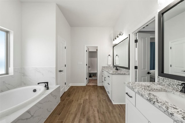 full bath with two vanities, a bath, wood finished floors, and a sink