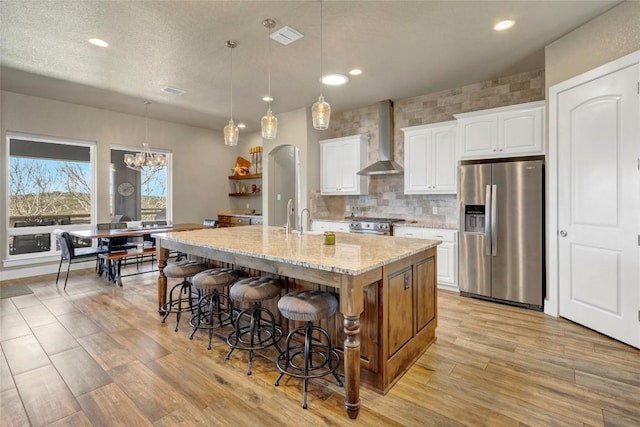 kitchen with wall chimney range hood, a kitchen breakfast bar, appliances with stainless steel finishes, arched walkways, and white cabinetry