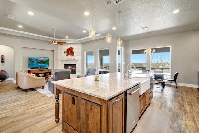 kitchen featuring brown cabinetry, visible vents, a tray ceiling, light wood-style flooring, and dishwasher