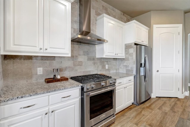 kitchen featuring wall chimney range hood, light stone countertops, tasteful backsplash, and appliances with stainless steel finishes