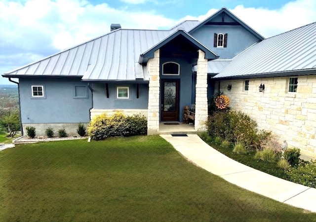 view of front facade with a front yard, stucco siding, metal roof, stone siding, and a standing seam roof