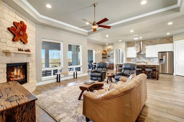 living area with a stone fireplace, light wood-style flooring, crown molding, and a tray ceiling