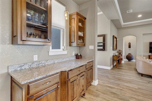 interior space with visible vents, light wood-style flooring, arched walkways, glass insert cabinets, and pendant lighting