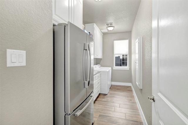 kitchen featuring a textured ceiling, washing machine and dryer, white cabinetry, freestanding refrigerator, and a textured wall