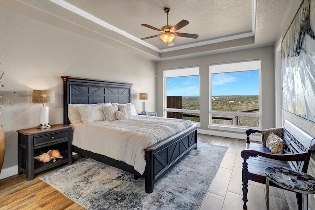 bedroom featuring ceiling fan, a tray ceiling, ornamental molding, light wood-style floors, and a textured ceiling