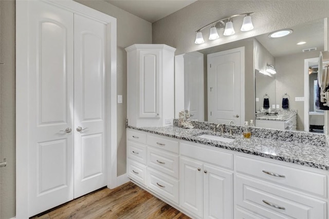 full bath with a closet, visible vents, vanity, and wood finished floors