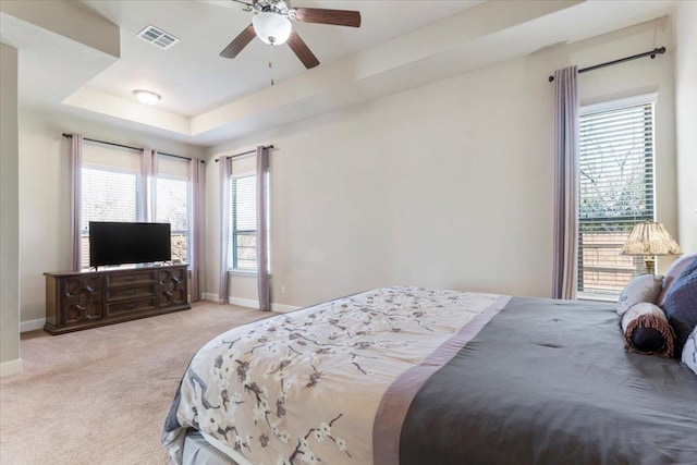 carpeted bedroom featuring baseboards, a tray ceiling, multiple windows, and visible vents