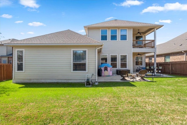 back of house with a balcony, a fenced backyard, a ceiling fan, and a lawn