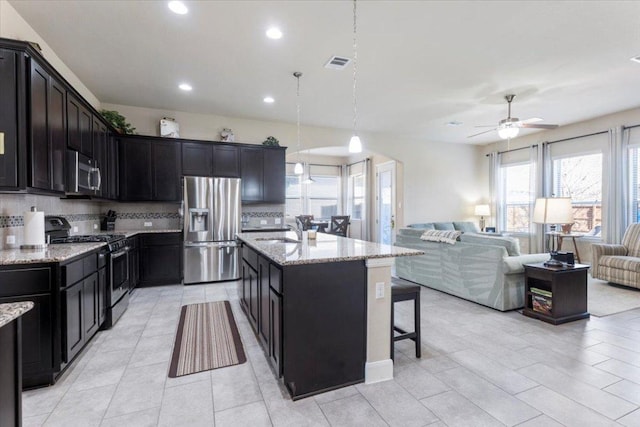 kitchen with a sink, light stone counters, a kitchen breakfast bar, open floor plan, and stainless steel appliances