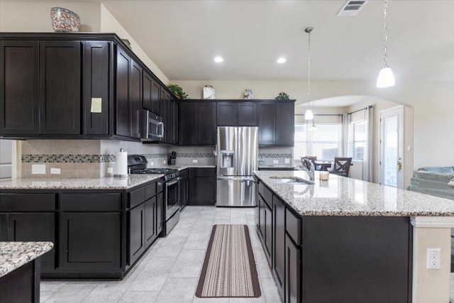 kitchen featuring light stone countertops, visible vents, arched walkways, a sink, and appliances with stainless steel finishes