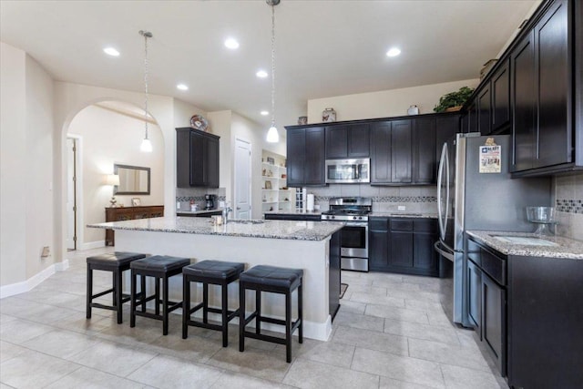 kitchen featuring light stone countertops, a kitchen bar, appliances with stainless steel finishes, arched walkways, and a sink