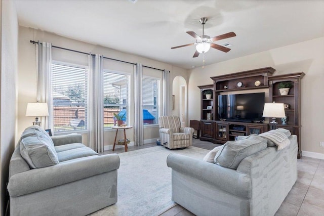 living room featuring baseboards, arched walkways, light tile patterned flooring, and a ceiling fan