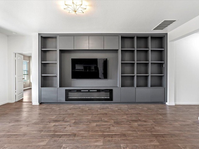 unfurnished living room with visible vents, built in features, a glass covered fireplace, and wood finished floors